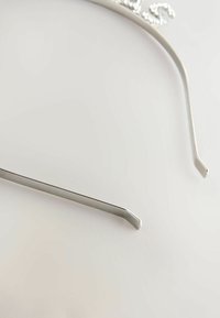 Sølv metal hårbånd med et slankt, moderne design. Har dekorerede kanter og let buede stænger for komfort.