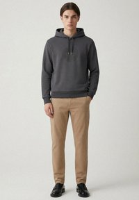 Grå huvtröja med en rund logotyp, justerbar dragsko och ribbade muddar, kombinerad med beige chinos och svarta loafers. Slät textur och avslappnad passform.