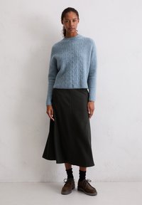 Hellblaues Kabelstrickpullover, dunkelgrüner Midirock, schwarze Socken und braune Schnürschuhe. Glatte Texturen und einfaches Design.