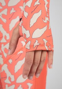 Langsleeve kledingstuk met een koraalpatroon en lichte romige abstracte vormen, met duim-gaatje manchetten en een rekbare stofstructuur.