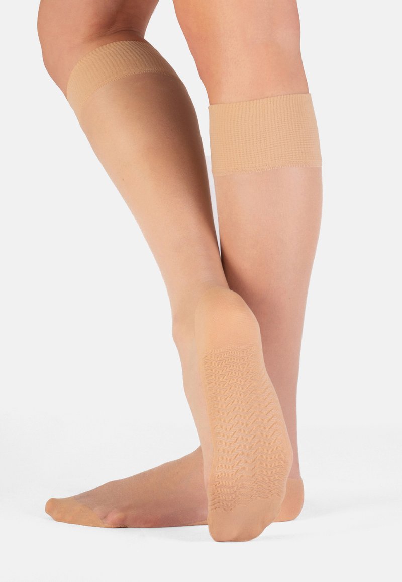 Medias beiges hasta la rodilla con una banda superior acanalada, textura transparente y suela antideslizante con patrón para estabilidad y confort.