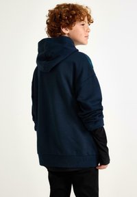 Marineblauwe hoodie van een zacht materiaal, met een ruime pasvorm, lange mouwen en subtiele ontwerpelementen op de schouders.