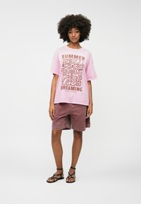 Pink oversized t-shirt with "SUMMER DREAMING" print, paired with rust-colored corduroy shorts and black strappy sandals.