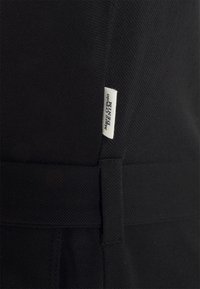 Czarnia tkanina o fakturowanym wykończeniu, z widocznym szwem i małą metką z napisem "Magic Opolo Denim" w kolorze białym.