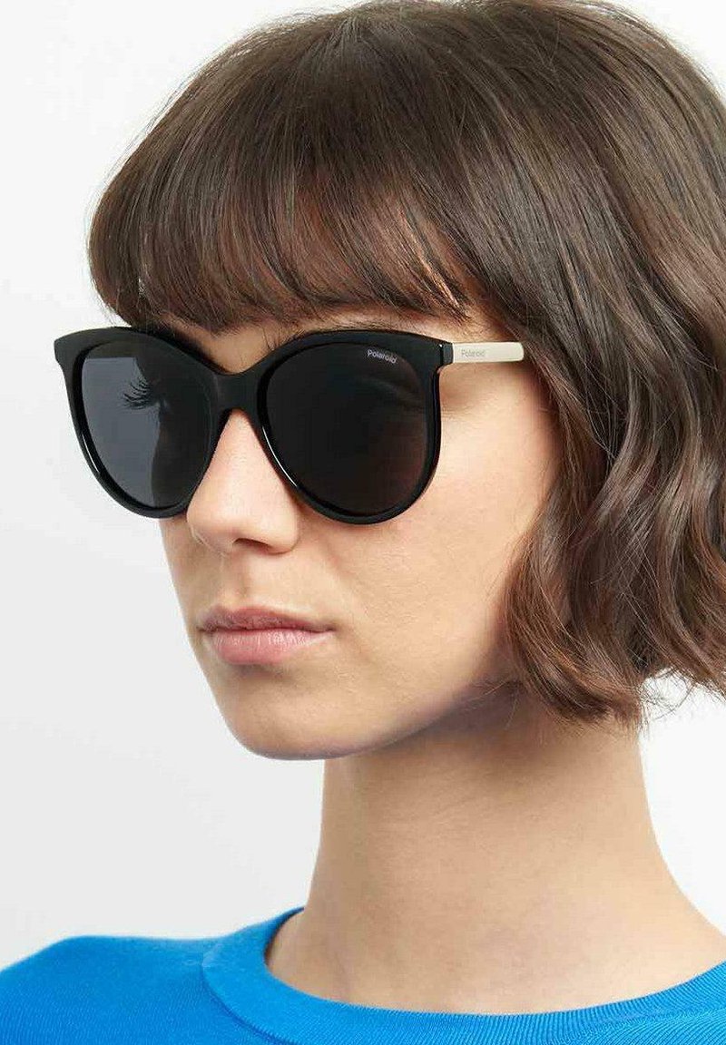 Occhiali da sole neri oversize con una montatura spessa e lenti scure. Accenti bianchi sui lati con il nome del marchio, Polaroid.
