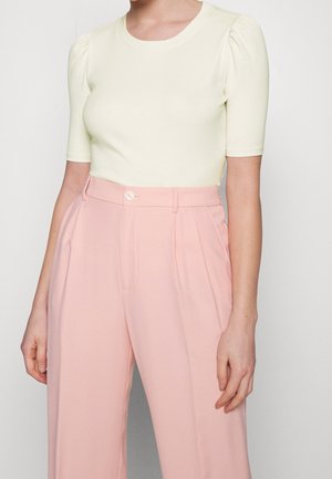 Kobieta ubrana w kremowy prążkowany top z krótkim rękawem z bufkami, włożony do wysokociśnieniowych, plisowanych różowych spodni o szerokich nogawkach.