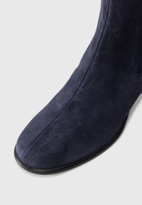 Navy blue suede ankle boot with a smooth texture, tapered toe, and black rubber sole, featuring a side elastic panel for easy wear.