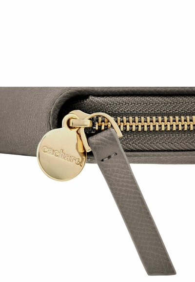 Tirette de fermeture éclair circulaire en or gravée "cacharel" attachée à une languette de fermeture éclair en cuir texturé gris sur une pochette en tissu assorti.