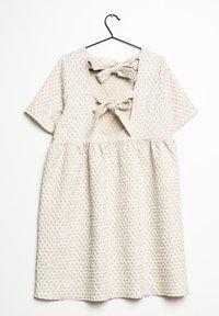 Beige strukturerad klänning med korta ärmar, med en rundad halsringning och två rosetter på baksidan. Prickig foder är synligt.
