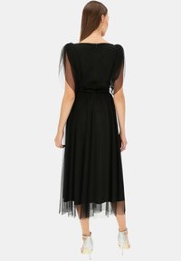 Czarna sukienka z przezroczystymi rękawami z tiulu, dopasowaną talią i zwiewną spódnicą. Z tyłu znajduje się zamek błyskawiczny, a długość sukienki sięga do połowy łydki.