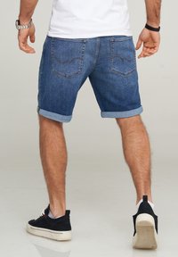 Jeansshorts i en medelblå nyans, med uppvikta benslut, bakfickor med sömdetaljer, och i kombination med svarta sneakers.