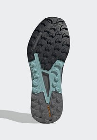 Suola di sneaker nera e grigia con scanalature profonde, caratterizzata da un accento turchese a forma di V e un logo in gomma. Superficie texturizzata per una migliore trazione.