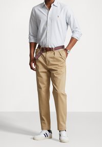 Button-up shirt in light blue and white stripes, tan chinos, multicolored striped belt, and white sneakers with blue accents.