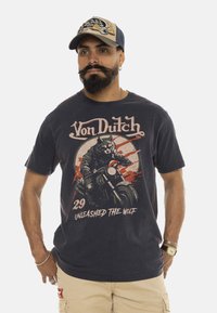 Camiseta de color azul marino con un gráfico de un lobo montando una motocicleta, con el texto "Von Dutch" y "Desata al Lobo" en colores contrastantes.