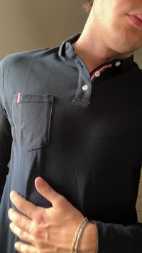 Marineblauw polo shirt met lange mouwen, gemaakt van gestructureerde stof. Het shirt heeft een borstzakje met een rood-wit gestreepte accent en twee knopen bij de kraag.