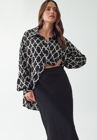 Camicia a maniche lunghe a fantasia bianca e nera, con chiusura a bottoni e vestibilità comoda, abbinata a una gonna nera semplice. Tessuto dalla consistenza liscia.