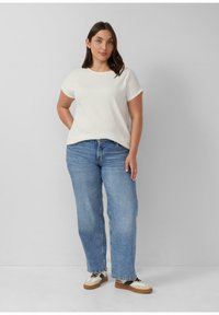 Witte textuur korte mouwen top gecombineerd met hoog-wasit lichtblauwe jeans en meerkleurige sneakers, wat een casual ensemble creëert.