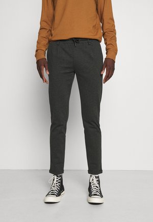 Pantalons gris fuselés en tissu doux, avec une taille élastique et des poches latérales, associés à des baskets montantes noires.