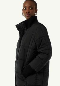 Czarna kurtka puchowa z pikowanym wzorem, wysokim kołnierzem, ściągaczami przy mankietach oraz bocznymi kieszeniami. Wykonana z gładkiego, ocieplanego materiału.