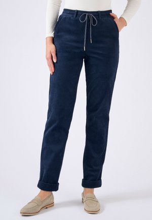 Pantaloni in velluto a coste blu navy con vita a coulisse e risvolti, caratterizzati da una superficie testurizzata e tasche laterali. Abbinati a mocassini di colore chiaro.