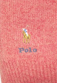 Tissu tricot rose avec logo brodé d'un joueur de polo à cheval au-dessus du mot « Polo » en couture bleue.