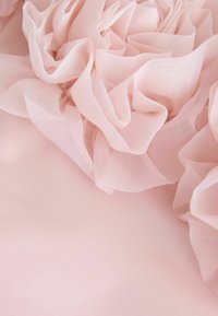 Tela de color rosa claro con volantes de tul suaves y en capas, con una textura delicada y transparente, sobre un fondo liso de color rosa.