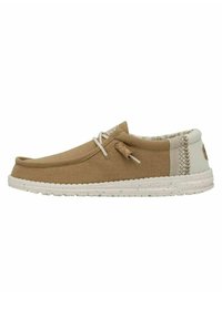 Zapato slip-on de lona marrón con suela de goma blanca, que presenta un panel trasero texturizado y un detalle decorativo de cordones en la parte delantera.