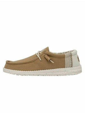 Zapato slip-on de lona marrón con suela de goma blanca, que presenta un panel trasero texturizado y un detalle decorativo de cordones en la parte delantera.