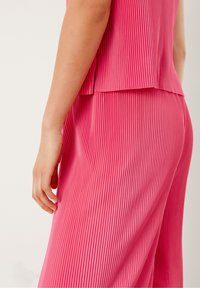 Conjunto de parte superior e inferior de color rosa con plisados verticales. La tela parece ligera, con una textura suave y un ajuste relajado.