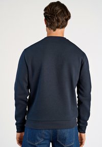 Granatowy sweter z okrągłym dekoltem, wykonany z mieszanki bawełny, z długimi rękawami oraz ściągaczami przy mankietach i u dołu. Posiada gładką fakturę i minimalistyczne wykończenie.