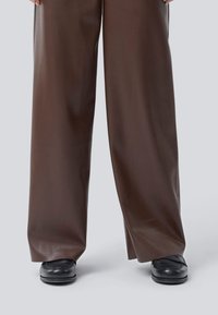 Braune weit geschnittene Hosen aus einem glänzenden, lederähnlichen Material; mit glatter Textur, hoher Taille und kombiniert mit schwarzen Schuhen.
