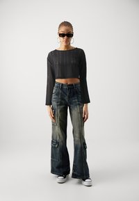 Black knitted crop top with long sleeves; wide cargo jeans with pockets; black sneakers; sunglasses; minimalist background.
