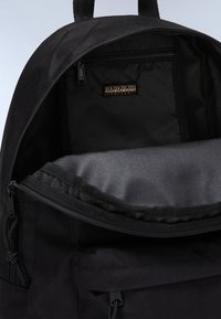 Zaino nero realizzato in un tessuto resistente. Presenta un compartimento principale con zip e una tasca interna. Design minimalista con un'etichetta del marchio discreta.