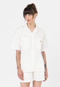 Camicia bianca a maniche corte, con bottoni sul davanti e due tasche sul petto. Tessuto morbido e leggero con un design semplice e un piccolo logo sulla tasca.