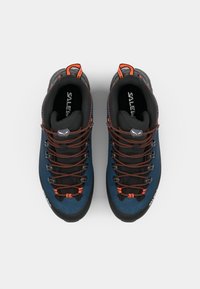 Blå og svarte klatresko med oransje lisser, teksturerte overdeler og gummisåler; har en logo på tungen og forsterket tåhette.