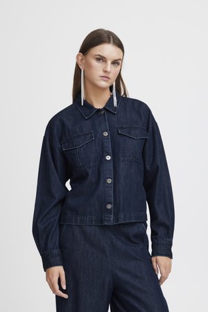 Mörkblå denimjacka med krage, knappstängning, två bröstfickor och långa ärmar. Slät textur med en kortad design.