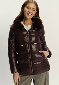 Burgunderfarbige Pufferjacke mit gestepptem Design, Kunstfellkragen, doppelten Trägern, Reißverschluss und Seitentaschen. Glatte, glänzende Textur.