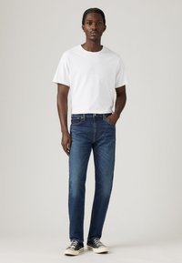 T-shirt bianco in cotone abbinato a jeans denim blu. Le scarpe sono nere con dettagli bianchi. Design semplice, vestibilità classica e colori solidi.