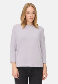 Lila, lange mouwen top met een bootnek. Zachte, gladde textuur. Losse pasvorm, gecombineerd met donkere broeken. Minimalistisch ontwerp, geen patronen.