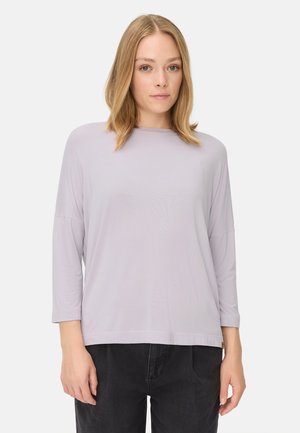 Lys lilla, langærmet bluse med bådhals. Blød, glat tekstur. Løs pasform, kombineret med mørke bukser. Minimalistisk design, ingen mønstre.