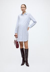 Lichtblauw gestreepte overhemdjurk met lange mouwen, knoopsluiting, zijdelingse strikjes, gecombineerd met glanzende zwarte kniehoge laarzen en een bordeauxrode handtas.