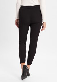 Leggings neri con vita alta, realizzati in un materiale elasticizzato. La vestibilità è affusolata, con linee pulite e senza tasche visibili.