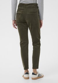 Oliven grøn fløjlsbukser med slim fit, der har baglommer og er parret med hvide sneakers på en neutral baggrund.