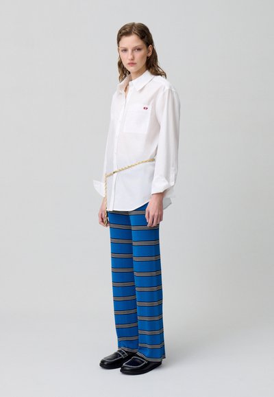 Camicia bianca con colletto, pantaloni palazzo a righe blu, scarpe nere con accenti argentati, cintura a catena dorata, texture liscia, silhouette casual.