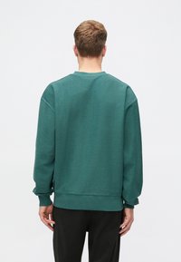 Zelená mikina s kulatým výstřihem z texturované látky, s kleslými rameny a žebrovanými manžetami. Vyznačuje se volným střihem a hladkým zadním designem.