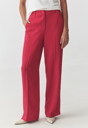 Rote weite Hosen aus leichtem Stoff, mit einer glatten Textur, seitlichen Taschen und einem plissierten Design. Kombiniert mit beigen spitzen Schuhen.