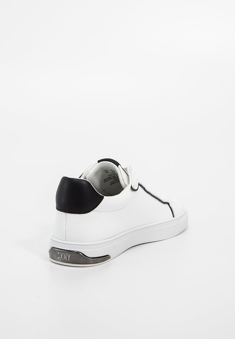 Witte leren sneaker met een zwart hielaccent en zilveren details op de zool. Heeft veters en een schoon, minimalistisch ontwerp.