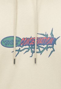 Tissu beige avec un motif abstrait vert et bleu comportant les mots "Volcom Stone Conservation" en lettres vertes et rouges.