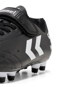 Sort fodboldstøvle lavet af syntetisk materiale med velcrolukning, hvide accenter, tekstureret overflade og formstøbte knopper for greb.