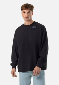 Black long-sleeve sweatshirt featuring a crew neck, loose fit, and chest embroidery in light blue with the text "PEGA DOR VALUES & VISIONS."